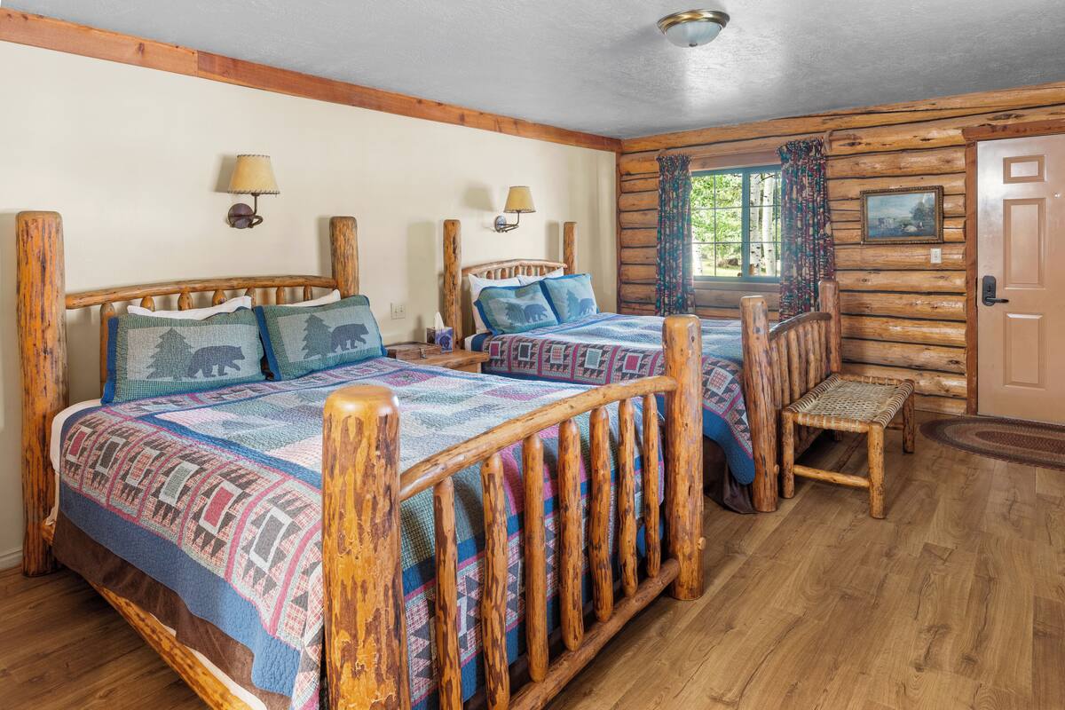 A log cabin-style bedroom with two wooden beds, a bench, and a door.