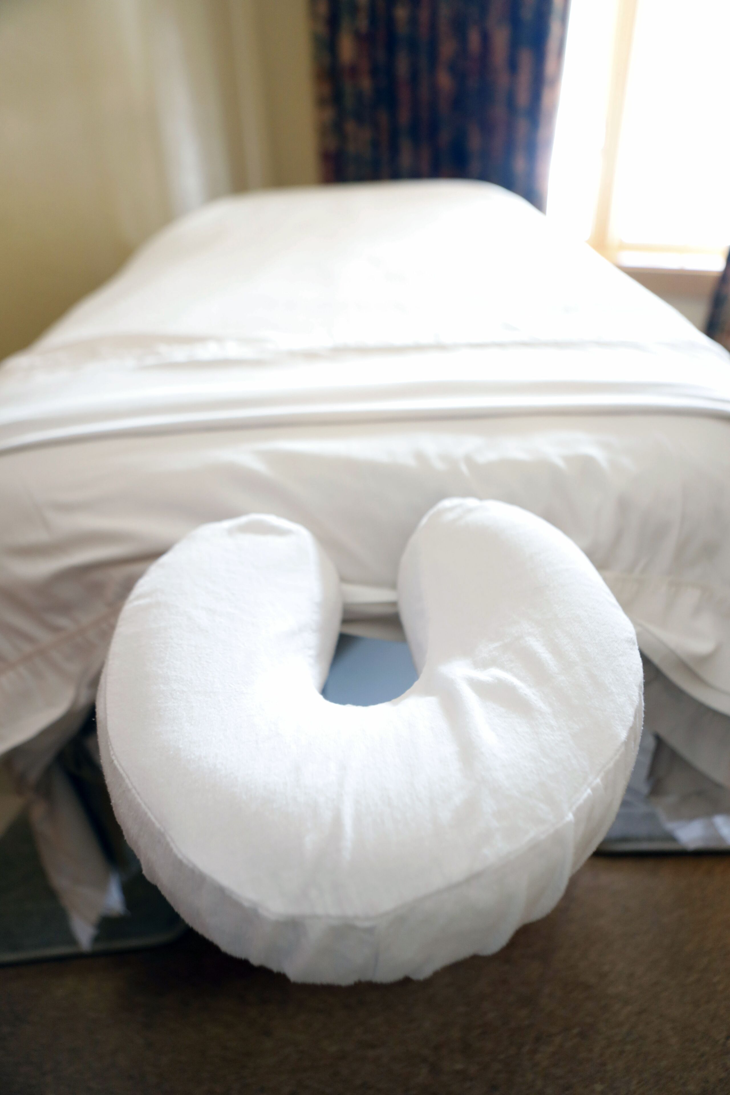 Ein weißes Nackenkissen auf einem Bett mit weißer Bettwäsche.