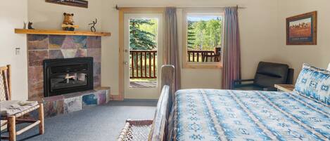 Ein Schlafzimmer mit Kamin, einem Bett mit gemusterten Betttextilien, einem Sessel und Blick ins Freie.