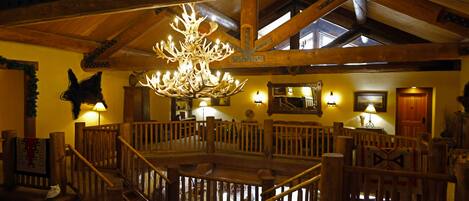 A spacious lobby with a high ceiling, wooden beams, a central chandelier, and a seating area with a wooden railing.