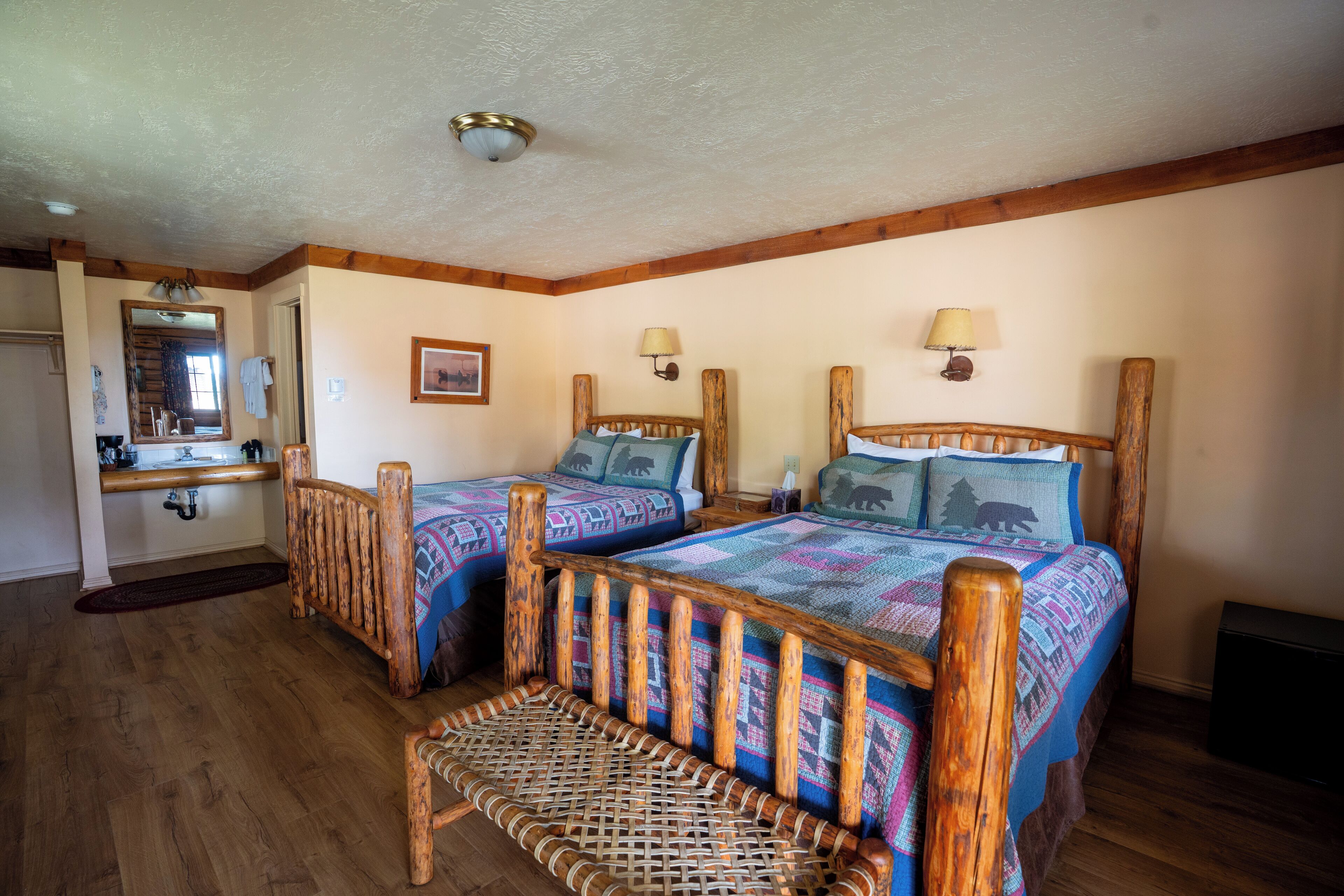 Un dormitorio con dos camas de madera, un banco tejido, un espejo y techo de madera.