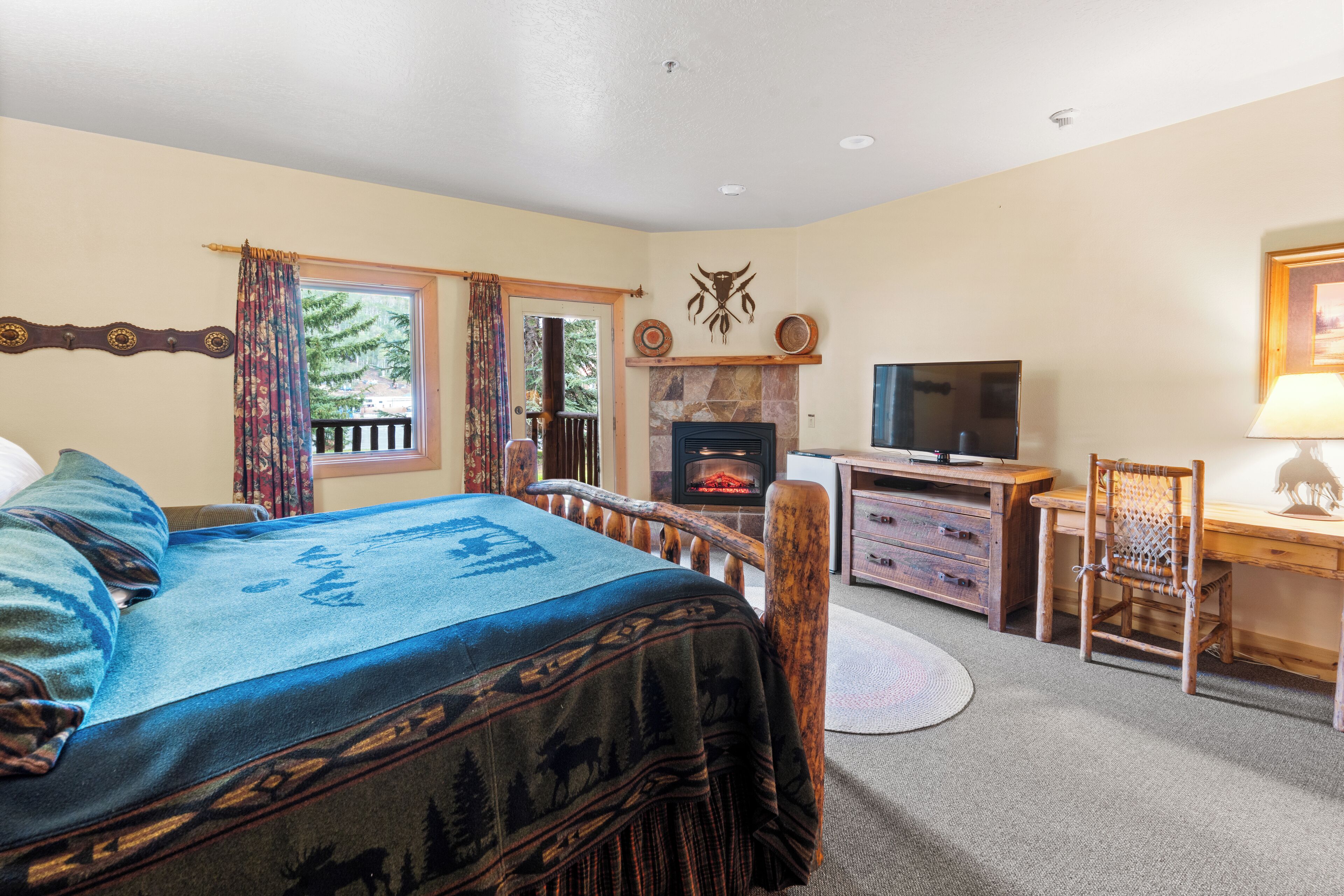 A bedroom with a bed, a wooden desk, a television, and a fireplace.