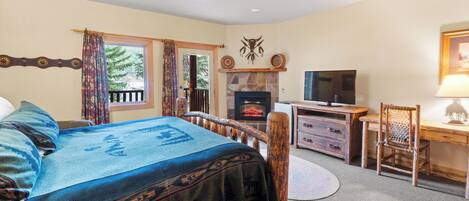 A bedroom with a bed, a wooden desk, a television, and a fireplace.