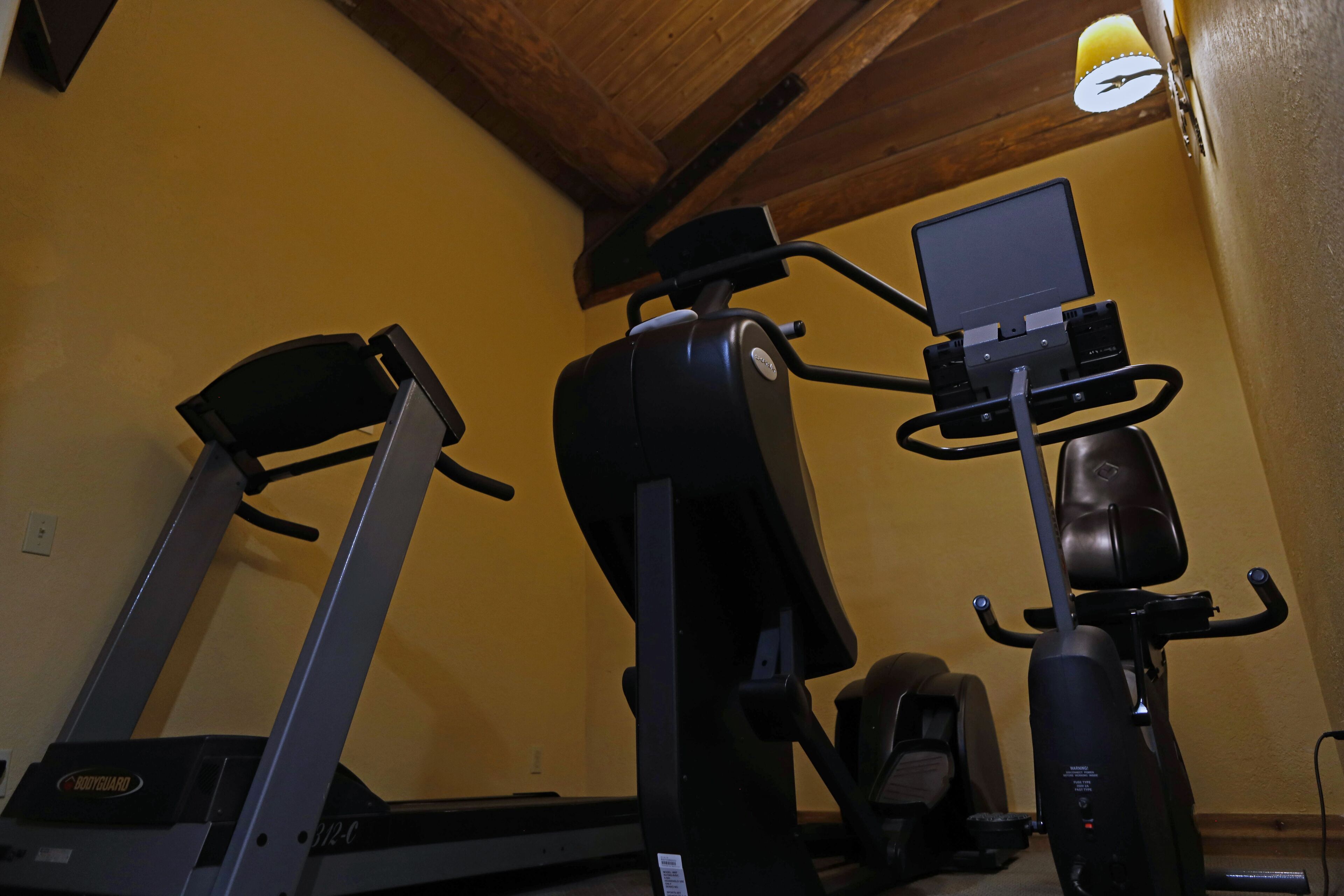 Une salle de sport à domicile équipée d’un tapis de course, d’un vélo elliptique et d’un vélo d’appartement.