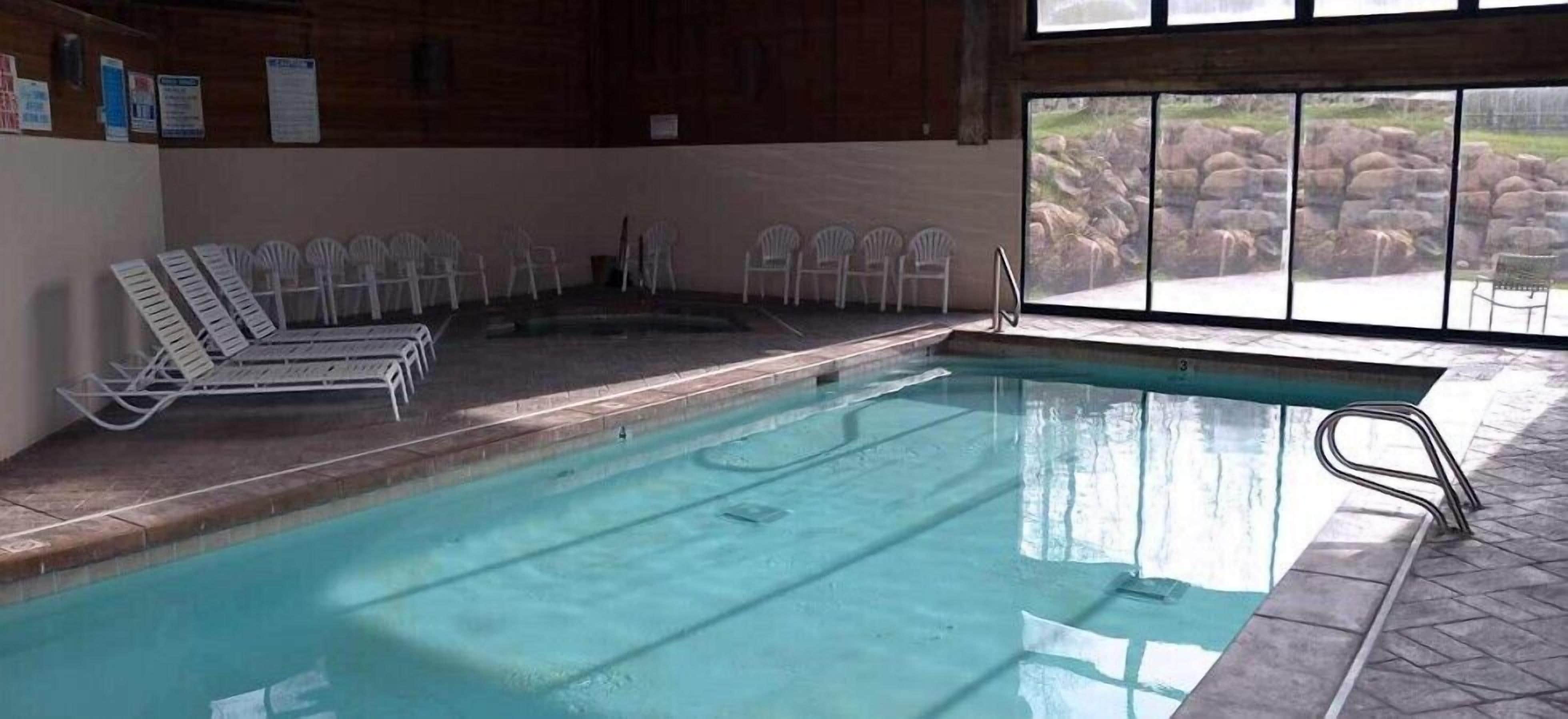 An indoor swimming pool with clear water, surrounded by white chairs and a stone wall.