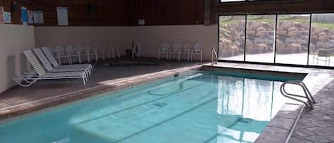 An indoor swimming pool with clear water, surrounded by white chairs and a stone wall.