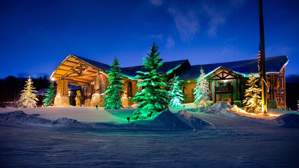 Eine Lodge mit Holzfassade, schneebedeckter Umgebung und beleuchteten Bäumen.