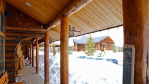 Eine verdeckte Holzterrasse mit Bänken, verschneiter Boden und eine Hütte im Hintergrund.