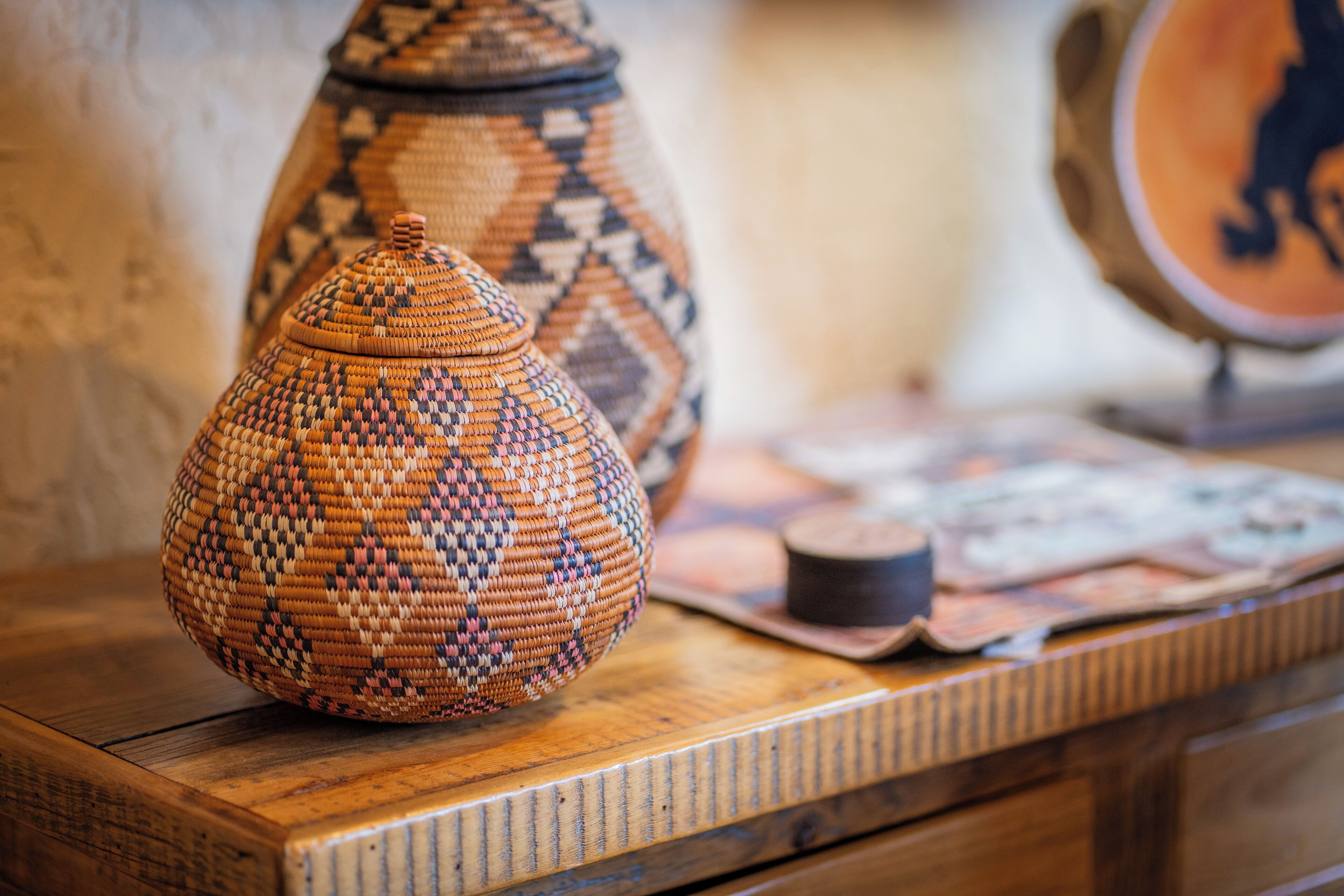 A woven basket on a wooden table with a patterned vase in the background.