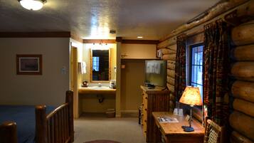A log cabin interior with a wooden dining table, a television, and a bathroom with a sink and mirror.