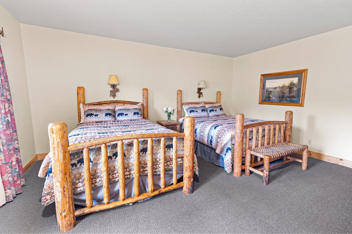 A room with two wooden beds, a bench, and a framed picture on the wall.
