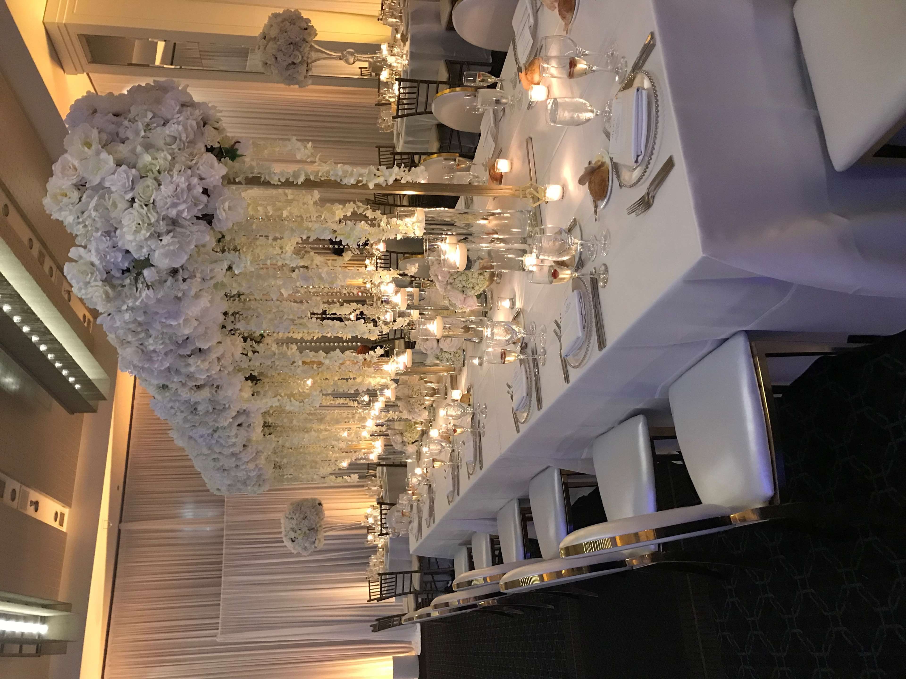 Un salón de banquetes con mesas largas dispuestas para un evento formal, decorado con arreglos florales y velas.