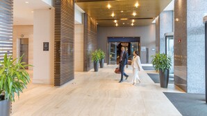 Un vestíbulo moderno con un revestimiento de madera en listones, plantas en macetas y piso de mármol.