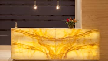 Un comptoir d’accueil avec un plateau en marbre, un vase rempli de fleurs et des luminaires suspendus.