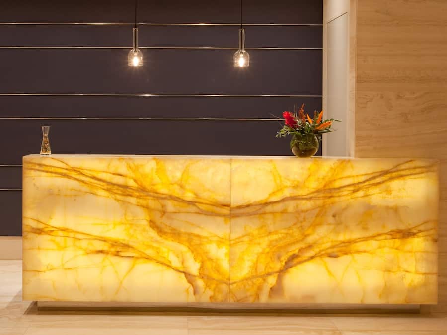 Un comptoir d’accueil avec un plateau en marbre, un vase rempli de fleurs et des luminaires suspendus.