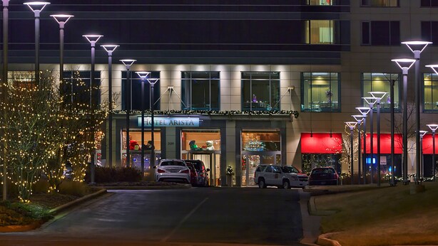 Entrada de hotel con un cartel que dice "HOTEL ARISTA", coches estacionados en la calle y luces decorativas.