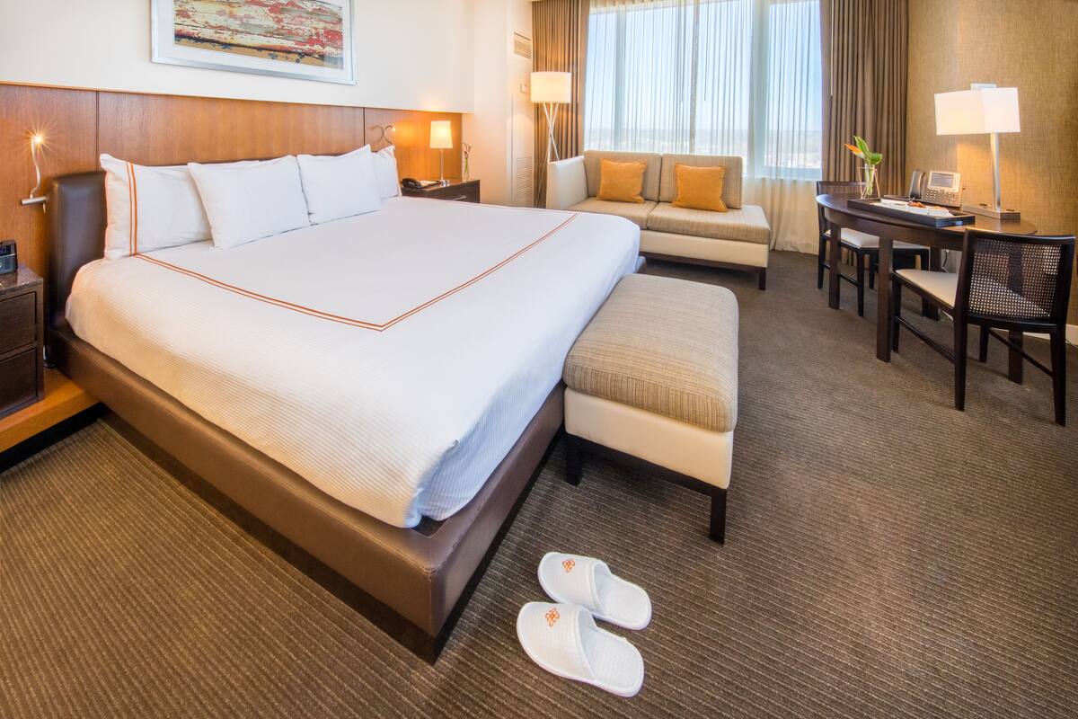A hotel room with a large bed, a sofa, a desk with a lamp, and a chair.