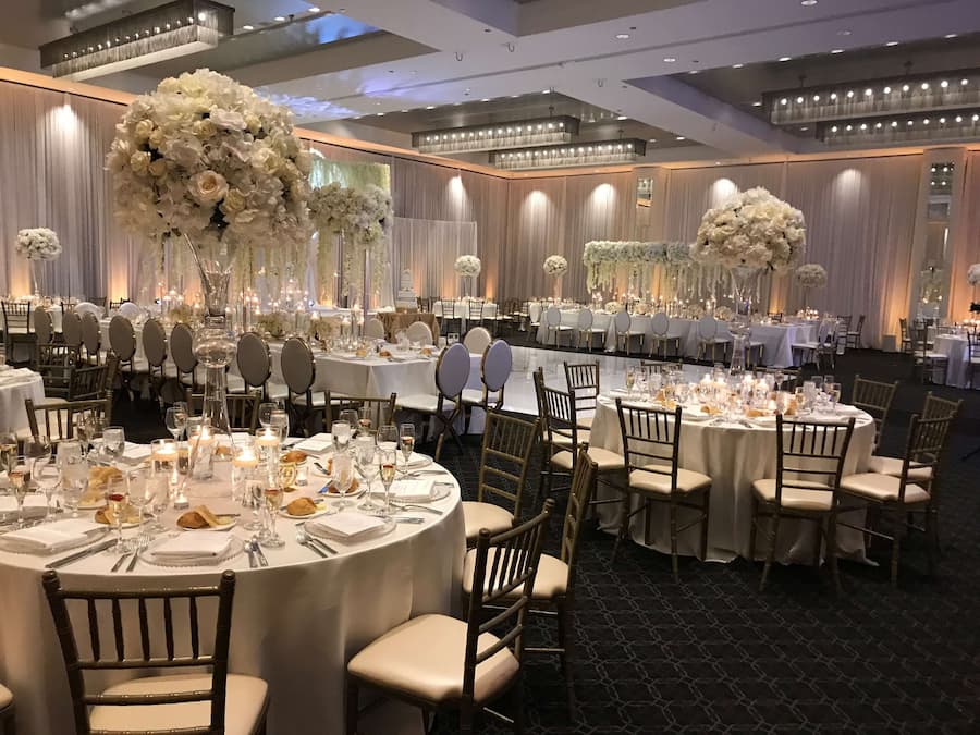 A banquet hall with round tables set for a formal event, featuring white floral arrangements and chandeliers.