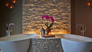 Un baño con dos tinas independientes, una pared decorativa de mosaicos y una planta ornamental con flores.