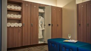 A hotel room with a large wardrobe, a seating area with a table, and neatly rolled towels on shelves.
