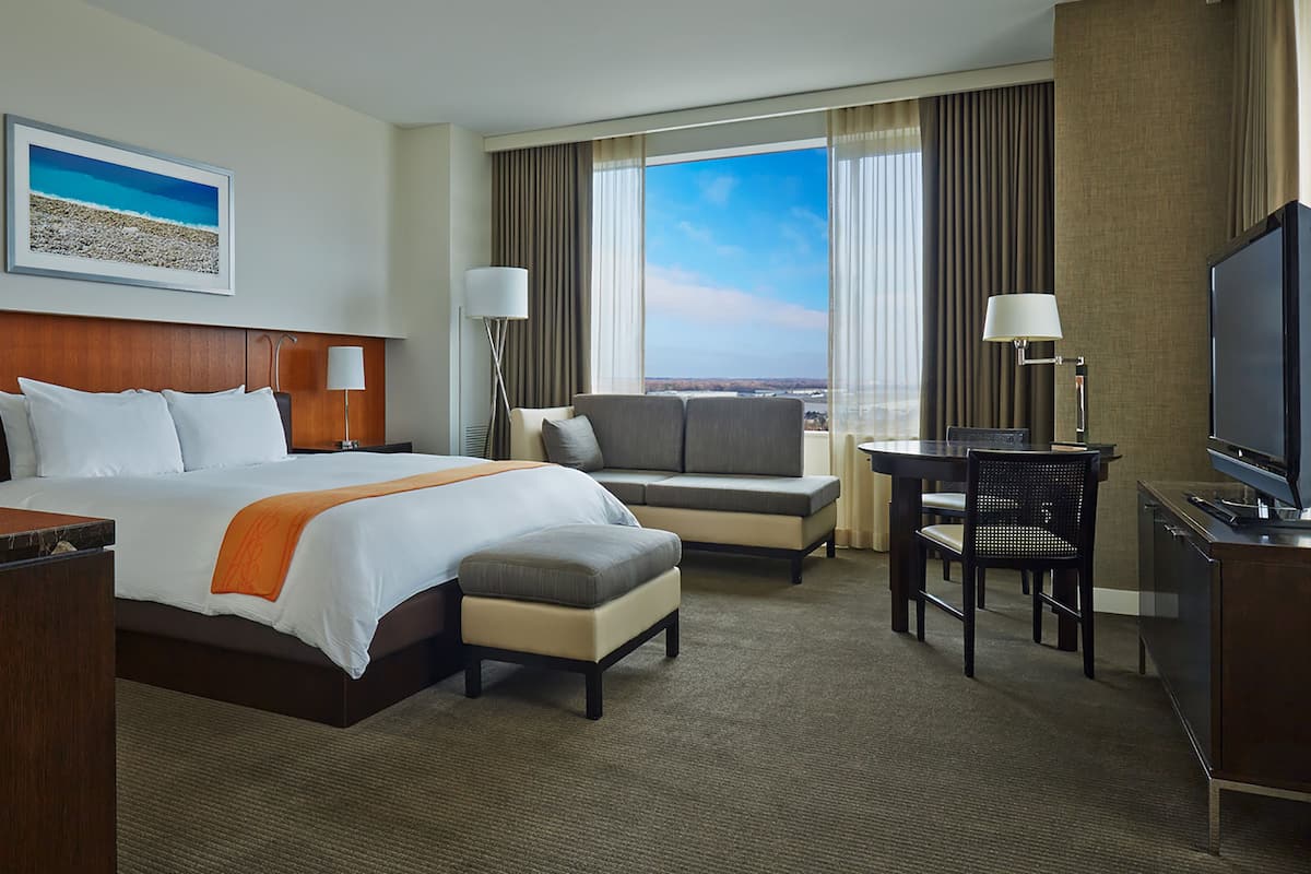 A hotel room with a bed, a sofa, a desk, a television, and a window with curtains.