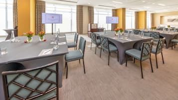Un salón de conferencias con varias mesas y sillas, amplias ventanas y un atril con pantalla.