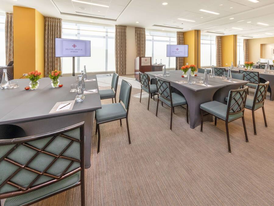 Un salón de conferencias con varias mesas y sillas, amplias ventanas y un atril con pantalla.