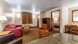 A hotel room with a red sofa, a small wooden table, a TV, and a desk with a chair. - Welcome Suites (O'Fallon)