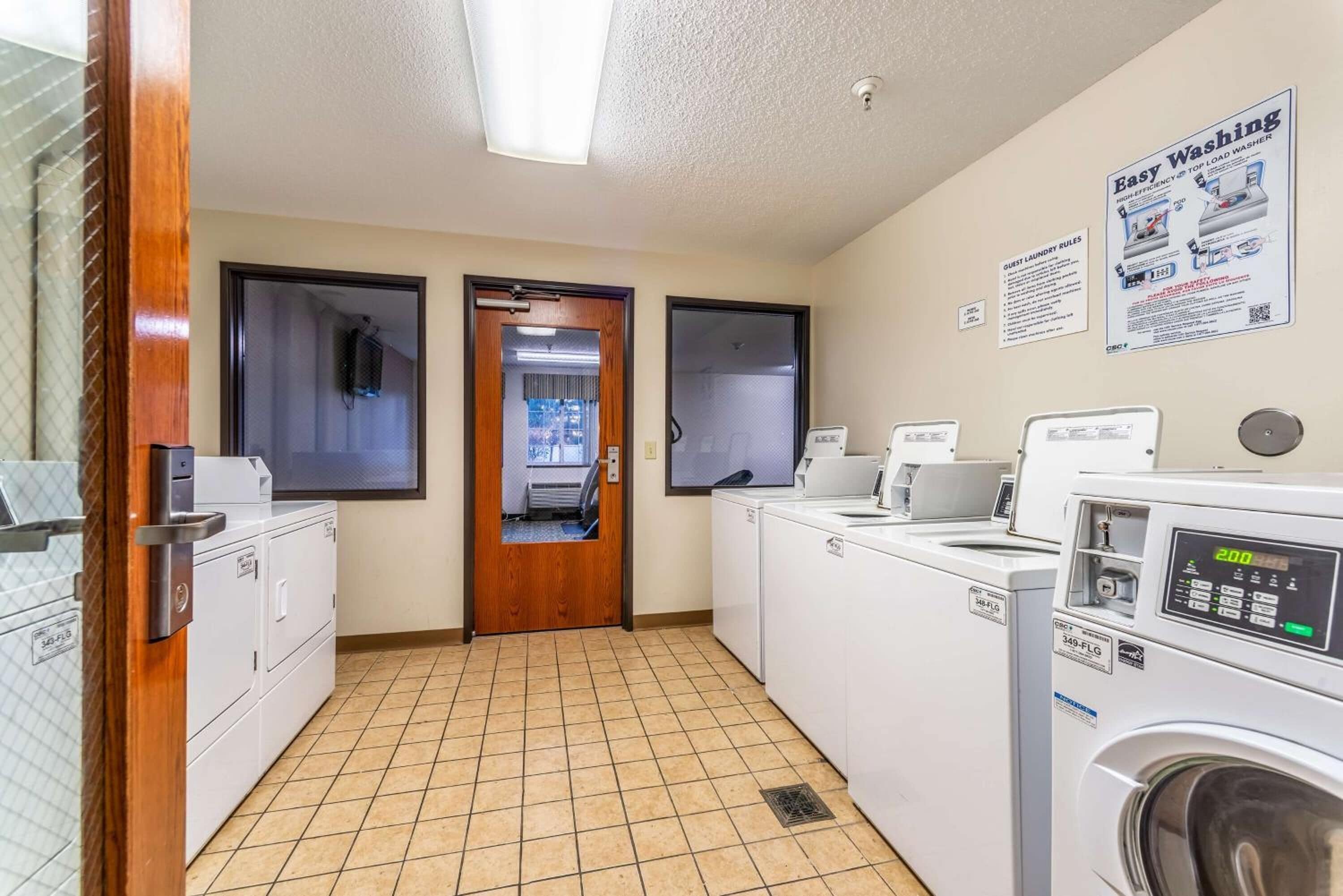 A laundry room with multiple washing machines, a dryer, and a door leading to another room.