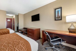 Habitación de hotel con dos camas, un escritorio, una silla, un televisor y una lámpara.
