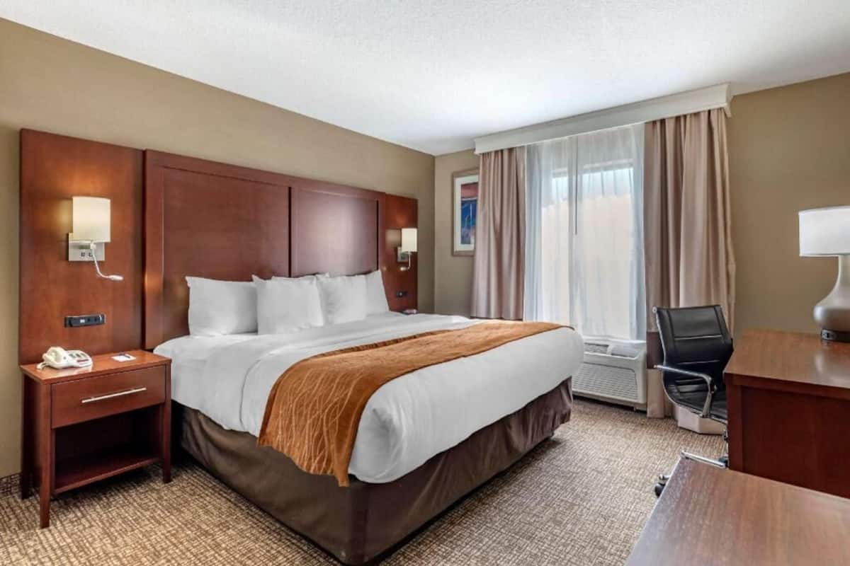 A hotel room with a large bed, a desk, a chair, a phone, and a window with curtains.