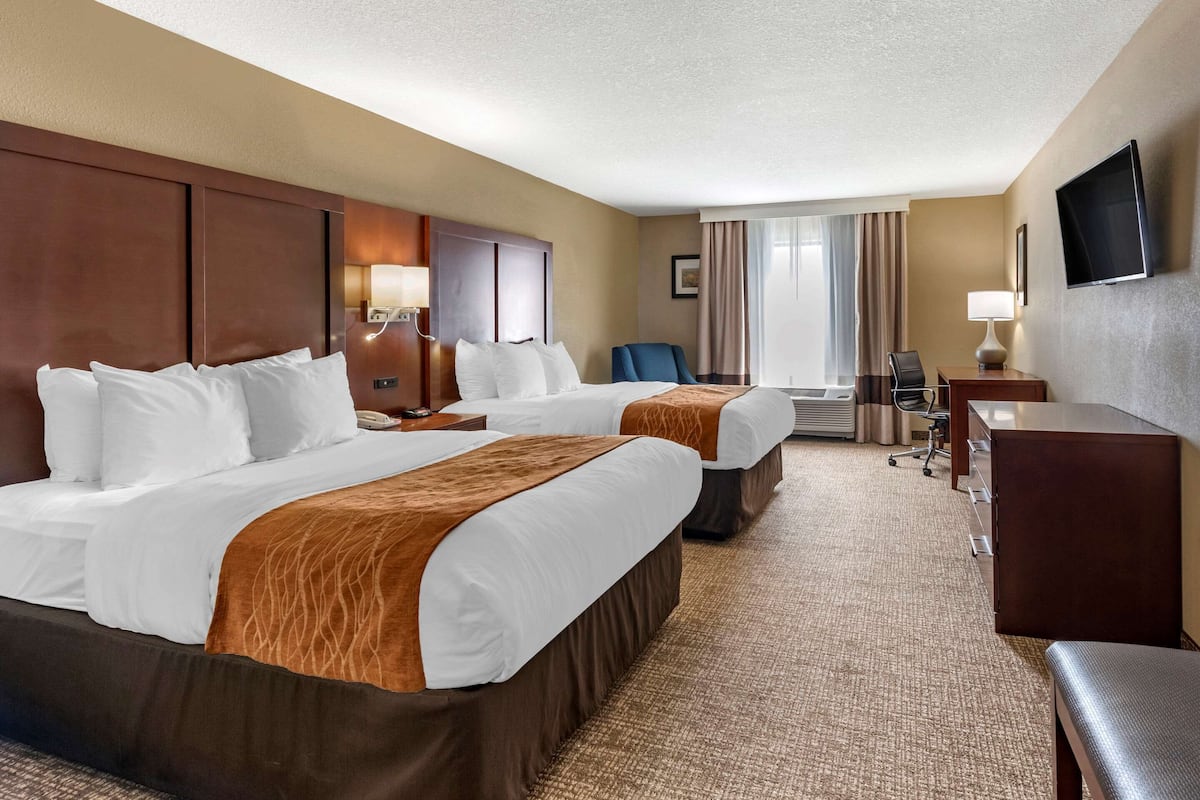 A hotel room with two beds, a desk, a chair, a TV, and a window with curtains.