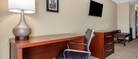 A hotel room with a desk, chair, lamp, TV, and a framed picture on the wall.