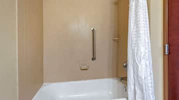 Un baño con una bañera blanca, ducha con barandilla y cortina de ducha blanca.
