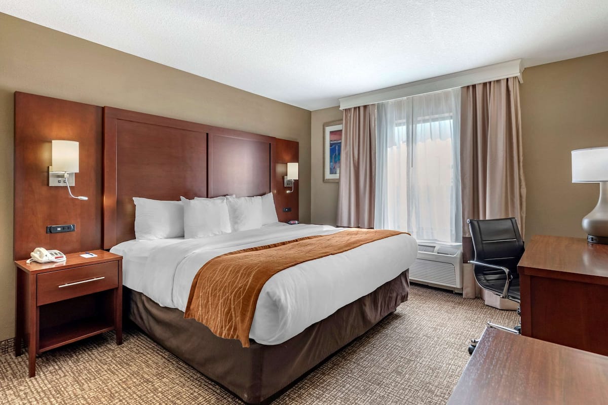 A hotel room with a large bed, bedside tables, a desk, and a chair.