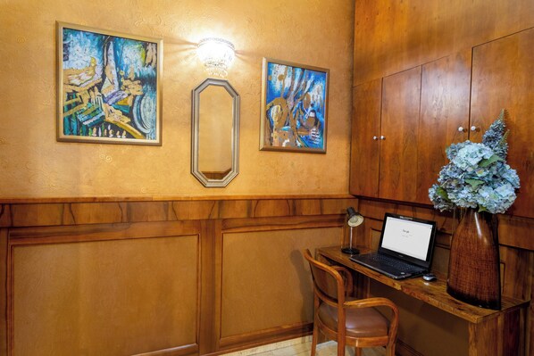 Un escritorio de madera con una computadora portátil, un florero con flores y dos cuadros en la pared.