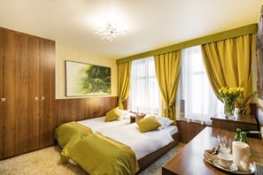 A hotel room with two beds, a wooden wardrobe, a desk with a vase of flowers, and a painting on the wall. - David Boutique Hotel (Kraków)