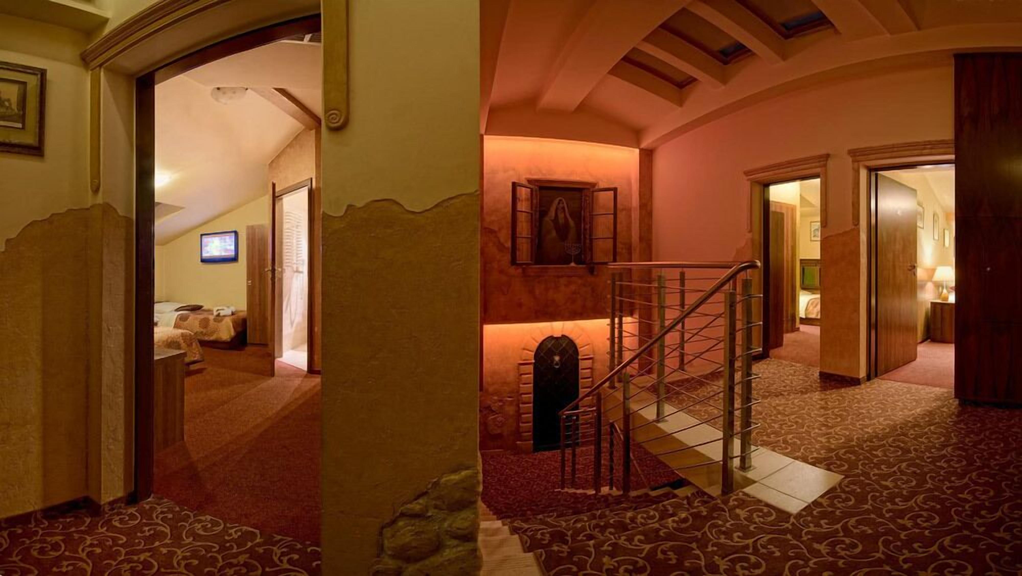 A hotel hallway with a staircase, a bed in the background, and a framed picture on the wall.
