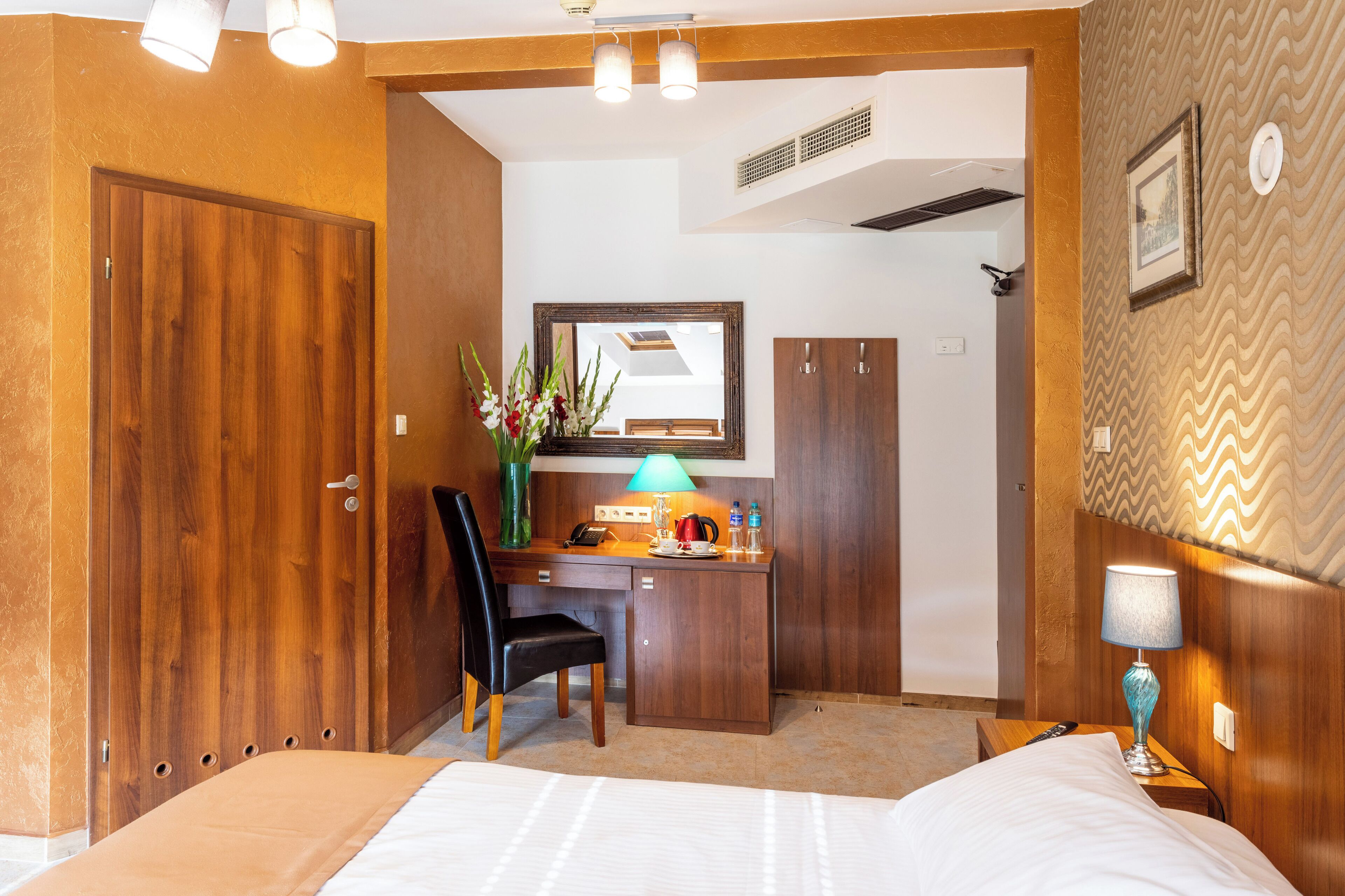 Una habitación de hotel con cama, escritorio, silla, lámpara de escritorio, espejo y armario.