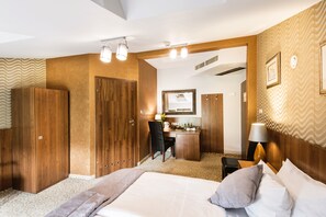 A hotel room with a large bed, a desk with a chair, a wardrobe, and a mirror. - David Boutique Hotel (Kraków)