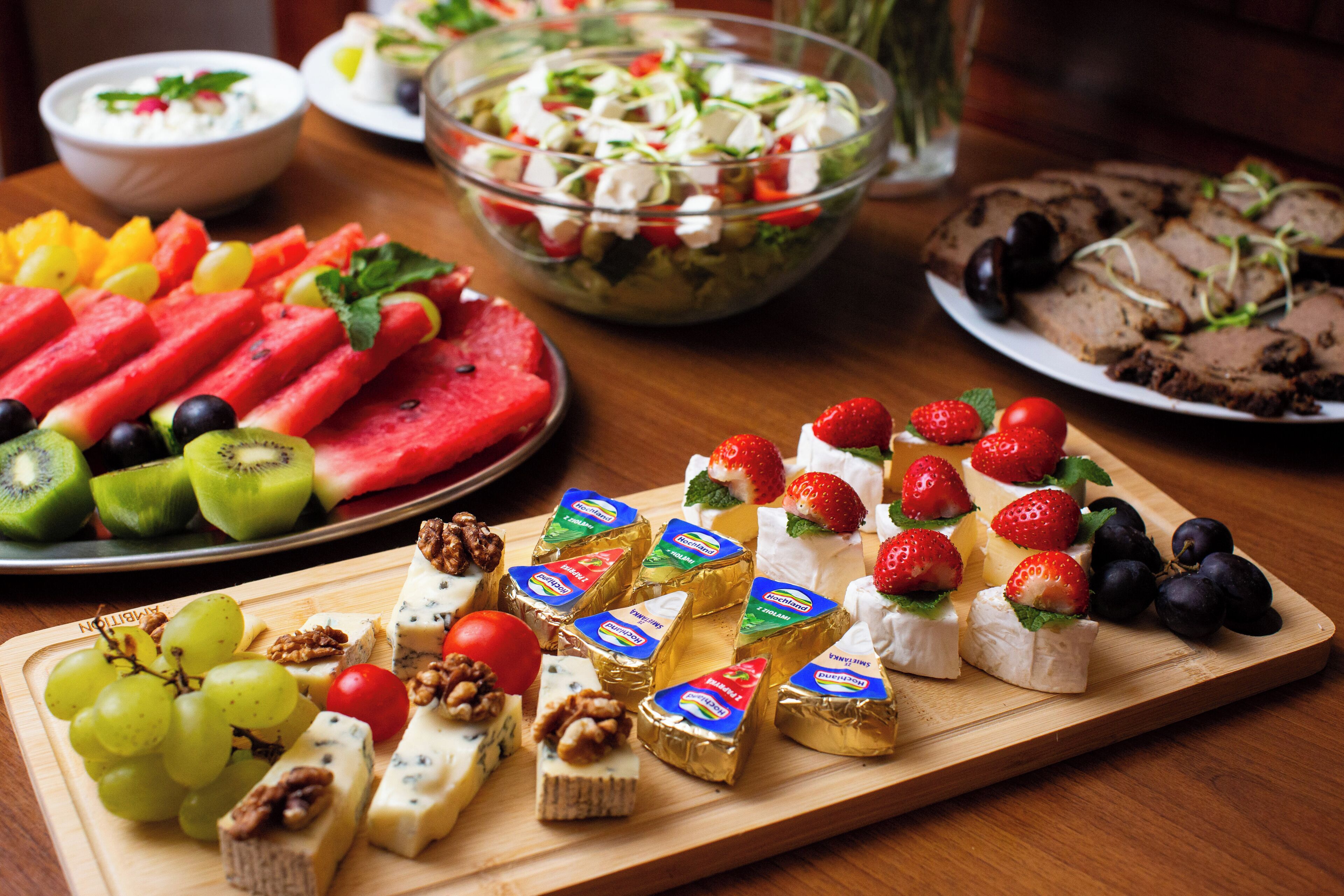 A variety of cheeses, fruits, and a salad on a wooden board.