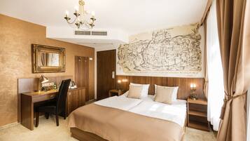 Quarto de hotel com uma cama grande, uma mesa, uma cadeira, luminária de mesa, mapa na parede e um lustre.