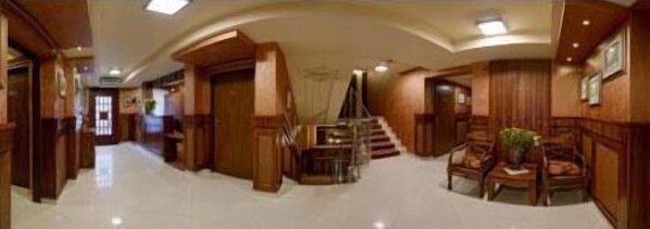 Un hall d’hôtel spacieux, agrémenté d’un grand escalier, de boiseries et d’un coin salon.