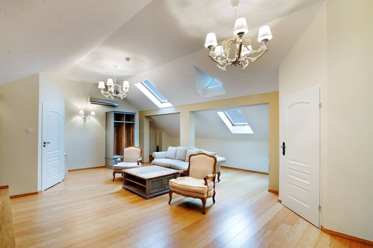A spacious loft with high ceilings, skylights, a chandelier, and a cozy seating area with a sofa and armchairs.