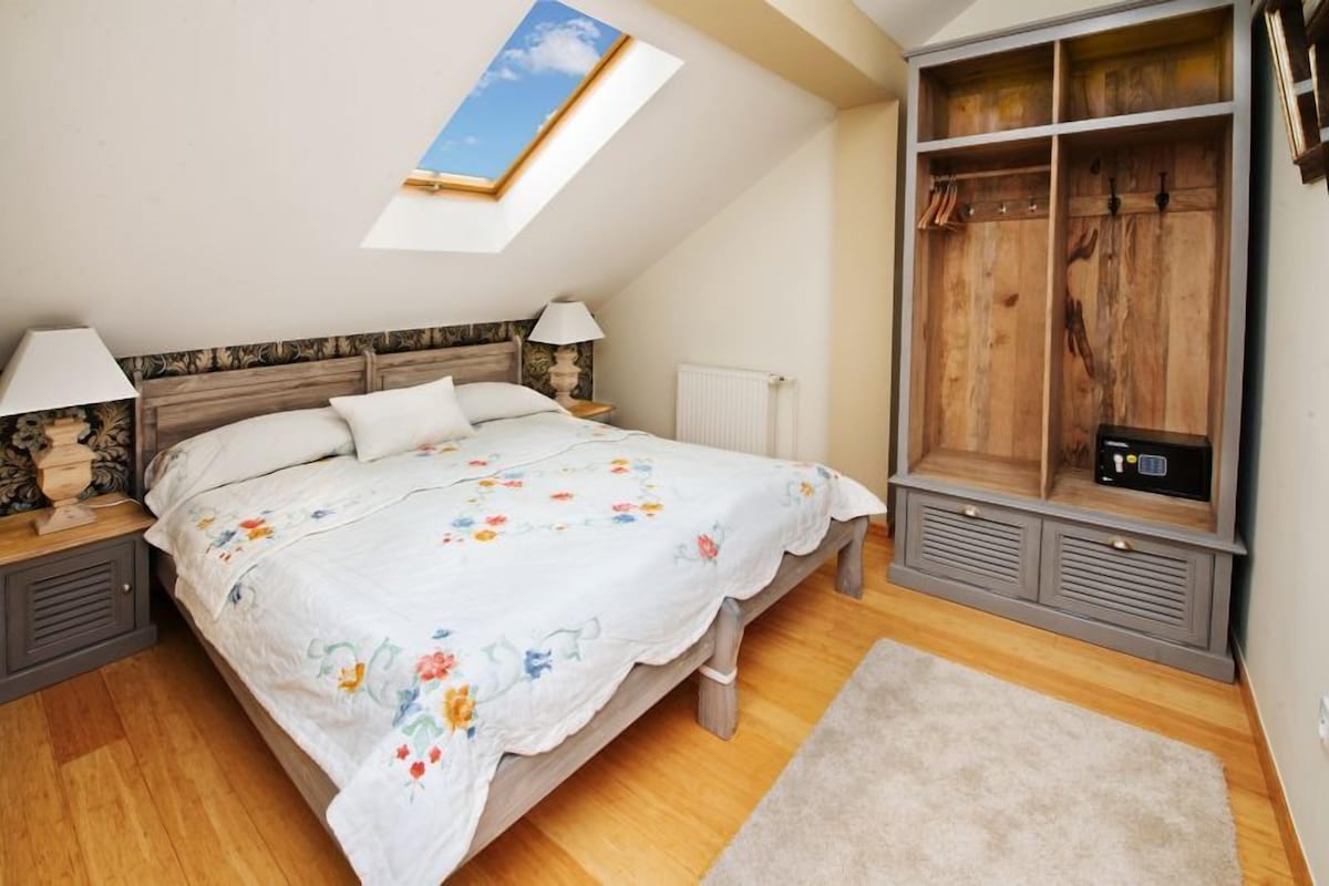 A bedroom with a skylight, a bed with floral bedding, a wooden wardrobe, and a radiator.