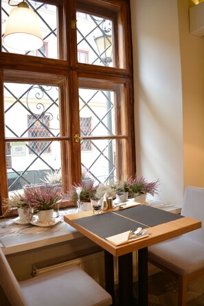 A dining area with a table set for two, a bench, and potted plants on the windowsill. - Hotel Mikołaj (Kraków)