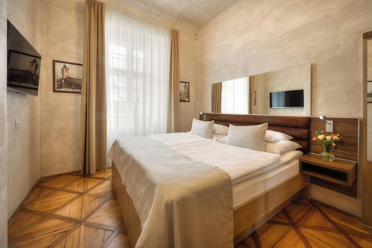 Quarto de hotel com uma cama grande, televisão, piso de madeira e janela com cortinas.