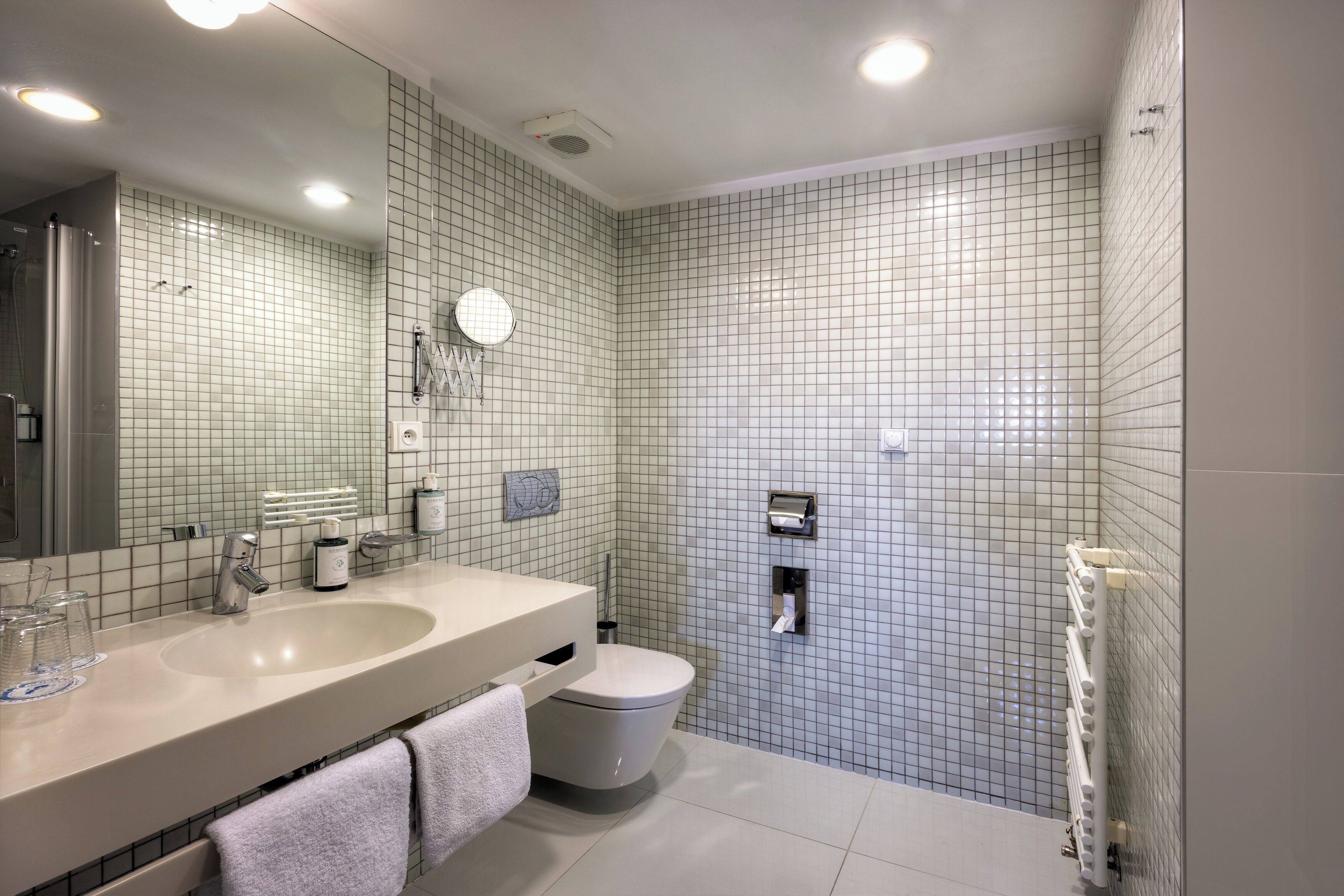 A modern bathroom with a large mirror, two sinks, a toilet, and a shower area.