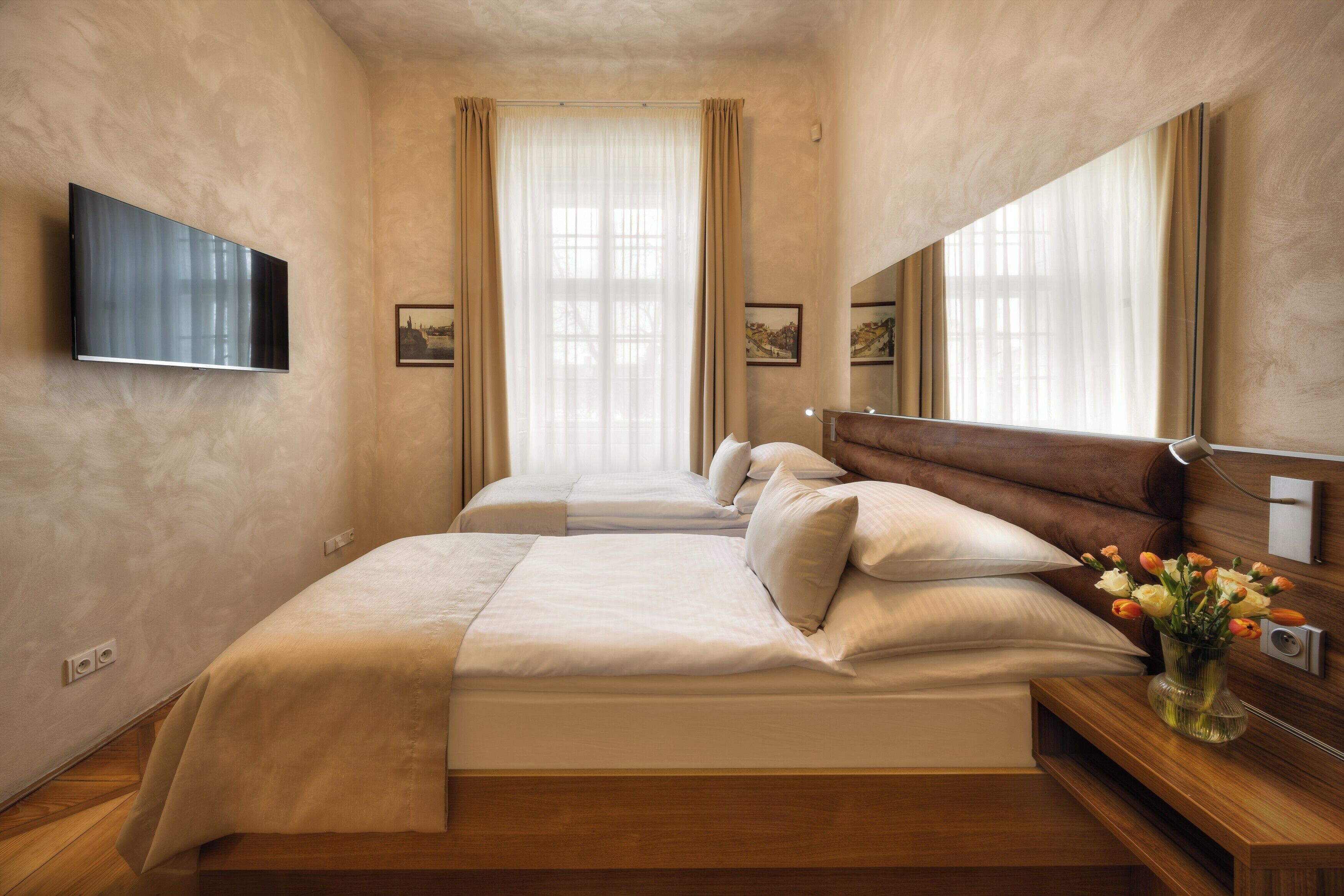 Ein Hotelzimmer mit einem großen Bett, einem an der Wand befestigten Fernseher und einem Nachttisch mit Blumen.