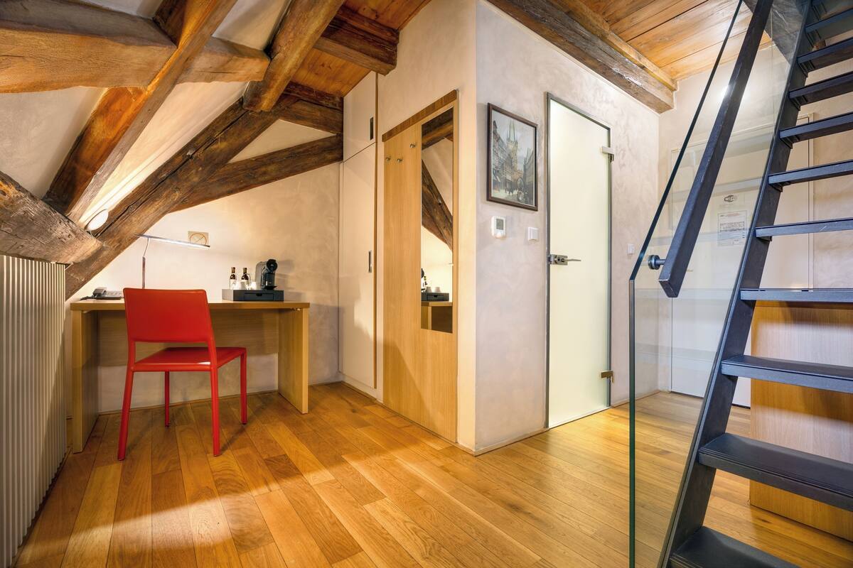 Quarto com escrivaninha de madeira, cadeira vermelha, escada e porta com um quadro emoldurado.
